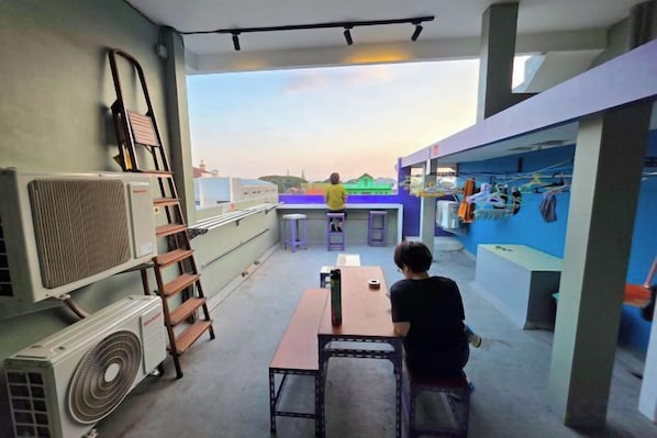 A rooftop terrace with a table and chairs, a ladder, and a fan. - Little Malang Hostel (Klojen)