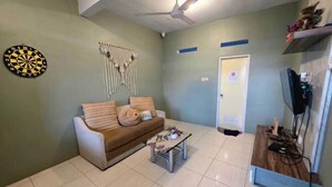 A living room with a sofa, a coffee table, a dartboard, and a wall-mounted TV. - Little Malang Hostel (Klojen)
