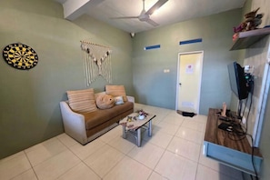 A living room with a sofa, a coffee table, a dartboard, and a wall-mounted TV. - Little Malang Hostel (Klojen)