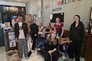 A hostel interior with a communal seating area, a notice board, and a wall with the hostel's name. - Little Malang Hostel (Klojen)