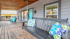 A covered porch with a wooden floor, a swing, and a bench with patterned cushions. - Walk to AT&T Stadium! | Dream City Retreat | 3BR/2BA w/Firepit & Modern Comforts (Arlington)