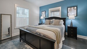 A bedroom with a bed, two bedside tables, a mirror, and a window with blinds. - Walk to AT&T Stadium! | Dream City Retreat | 3BR/2BA w/Firepit & Modern Comforts (Arlington)