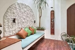 A room with a stone wall, a bench with cushions, a potted plant, and a wooden door. - Landmark Villas (Bali)