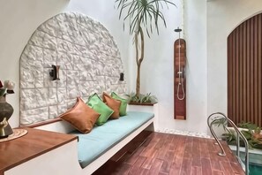 A room with a stone-textured wall, a bench with cushions, a potted plant, and a shower area. - Landmark Villas (Bali)