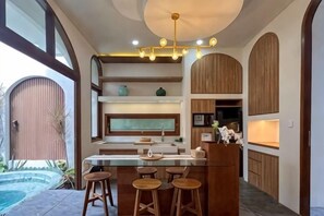 Une cuisine moderne avec un coin bar, des meubles en bois et une piscine visible au fond.