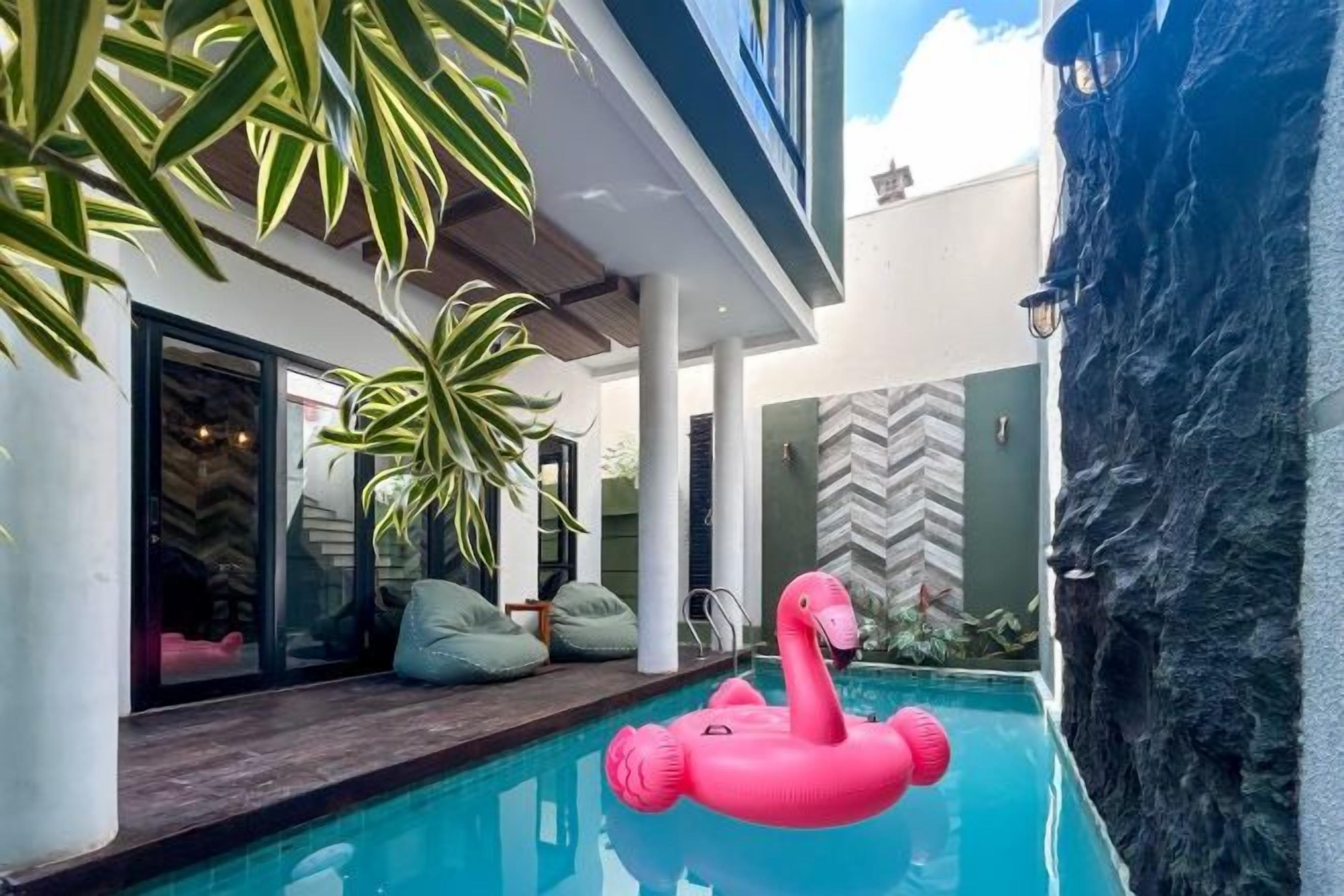A modern pool area with a pink flamingo float, indoor plants, and a stone wall.