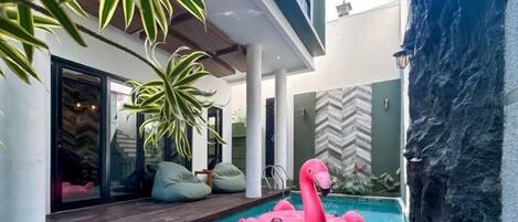 Un área de piscina moderna con un flotador de flamenco rosa, plantas de interior y una pared de piedra.