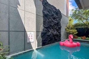 A swimming pool with a rock wall and a pink flamingo float. - Landmark Villas (Bali)