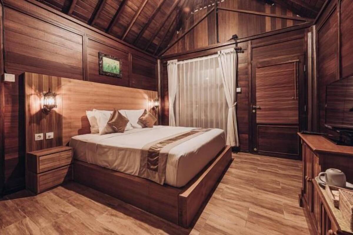 Un dormitorio con paneles de madera, una cama, mesitas de noche, un aparador y una ventana con cortinas.