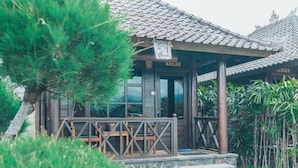A traditional wooden building with a tiled roof, a covered porch with wooden furniture, and a stone staircase leading to the entrance. - Kayu Manise Villa Bedugul (Bali)