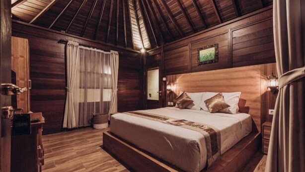 A wooden cabin bedroom with a large bed, wooden walls, and a sloped ceiling. - Kayu Manise Villa Bedugul (Bali)