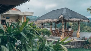 A thatched-roof gazebo with outdoor seating, surrounded by lush greenery and a view of a distant cityscape. - Kayu Manise Villa Bedugul (Bali)