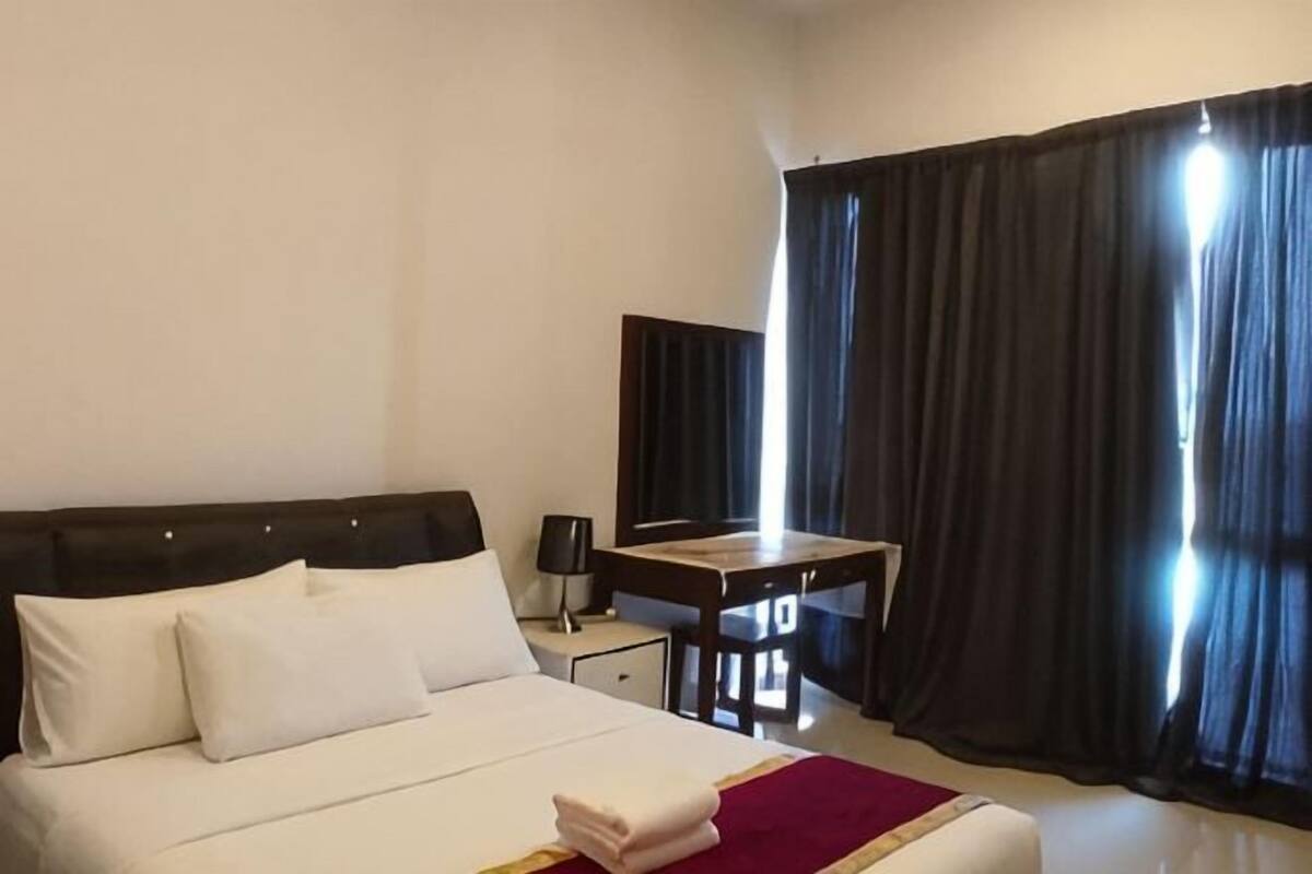 A hotel room with a bed, a desk, a chair, and a large window with curtains.
