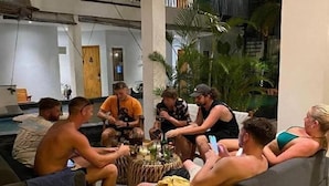 A group of people sitting around a table in a room with a pool, white walls, and plants. - Coco & Pineapple Pants Hostel (Bali)