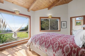 Une chambre avec une grande fenêtre, un lit recouvert d’une couvre-lit à motifs et un tableau encadré accroché au mur.