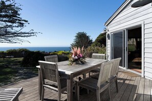 Une terrasse en bois avec une table et des chaises, offrant une vue panoramique sur l’océan.