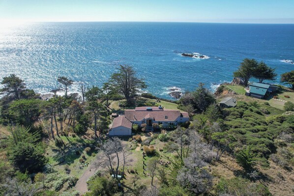 Une propriété située sur la côte, comprenant une maison principale et une dépendance plus petite, entourée d’une végétation luxuriante et offrant une vue sur l’océan.