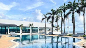A pool area with a tiled edge, lounge chairs, palm trees, and a building with large windows. - Chaolao Sea Breeze Resort (Tha Mai)