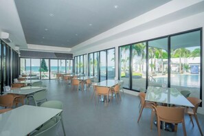 Un vaste espace intérieur aménagé en salle à manger, avec des tables et des chaises, de grandes fenêtres et une vue sur l’océan.