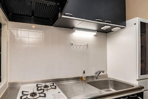 A kitchen with a gas stove, stainless steel sink, and black cabinets. - Rose Park Second House (Funabashi)
