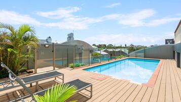 A rooftop pool area with lounge chairs, a glass-enclosed structure, and a clear blue sky.
