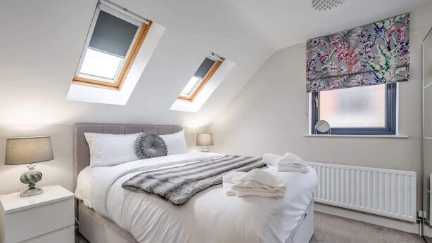 A bedroom with a bed, two bedside tables, a radiator, and skylights. - Utility Street - 1-bed Apt + Parking (Belfast)