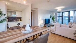 Uma sala de estar moderna com uma mesa de jantar de madeira, um sofá e uma televisão.