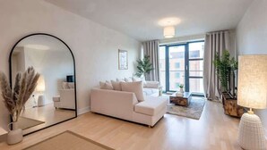 Uma sala de estar moderna com um espelho grande, um sofá branco, uma mesa de centro e um abajur.