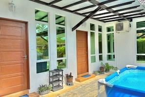 A covered outdoor area with a swimming pool, wooden doors, and large windows.