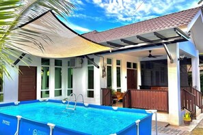 A swimming pool with a sunshade, a covered patio, and a house with large windows. - Tepak Nusuk Private Pool Homestay 5 Bedrooms 4 Bathrooms (Kota Bharu)