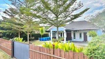 A modern house with a white exterior, a covered porch, and a fenced backyard with tropical plants.