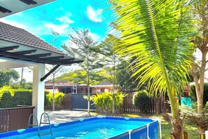 A swimming pool with a ladder, surrounded by palm trees and a covered patio area.