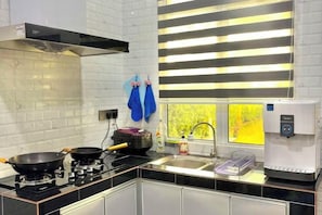 A modern kitchen with a gas stove, a coffee machine, and a window with blinds.