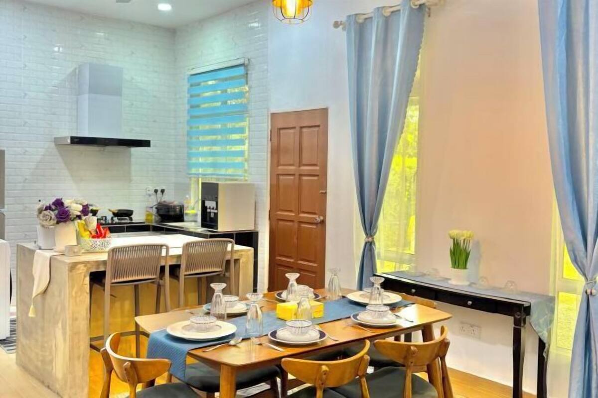 A modern kitchen with white brick walls, a wooden dining table set for four, and a view of the outdoors through a window with blue curtains.
