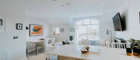 A modern kitchen with a central island, white furniture, and a large window providing natural light.
