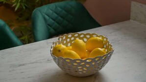 Un bol blanc orné d’un motif ajouré, contenant des citrons, posé sur une surface en marbre.