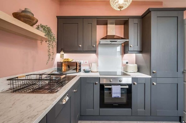 A modern kitchen with dark grey cabinets, a stainless steel range hood, a built-in oven, and a marble countertop.