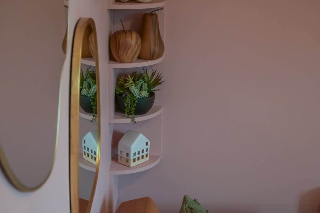 Une étagère d’angle agrémentée d’objets décoratifs, notamment deux vases en bois, une petite plante en pot et une maquette de maison miniature.