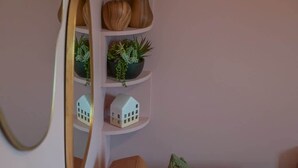Une étagère d’angle agrémentée d’objets décoratifs, notamment deux vases en bois, une petite plante en pot et une maquette de maison miniature.