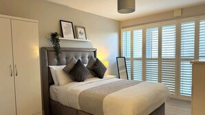 Une chambre à coucher comprenant un lit, une armoire, une table de chevet et une fenêtre avec des stores.