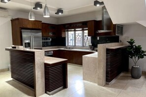 A modern kitchen with a central island, built-in appliances, pendant lighting, and a large window providing natural light. - Kim’s House Entire Villa 6-BR Near My Khe Beach (Da Nang)