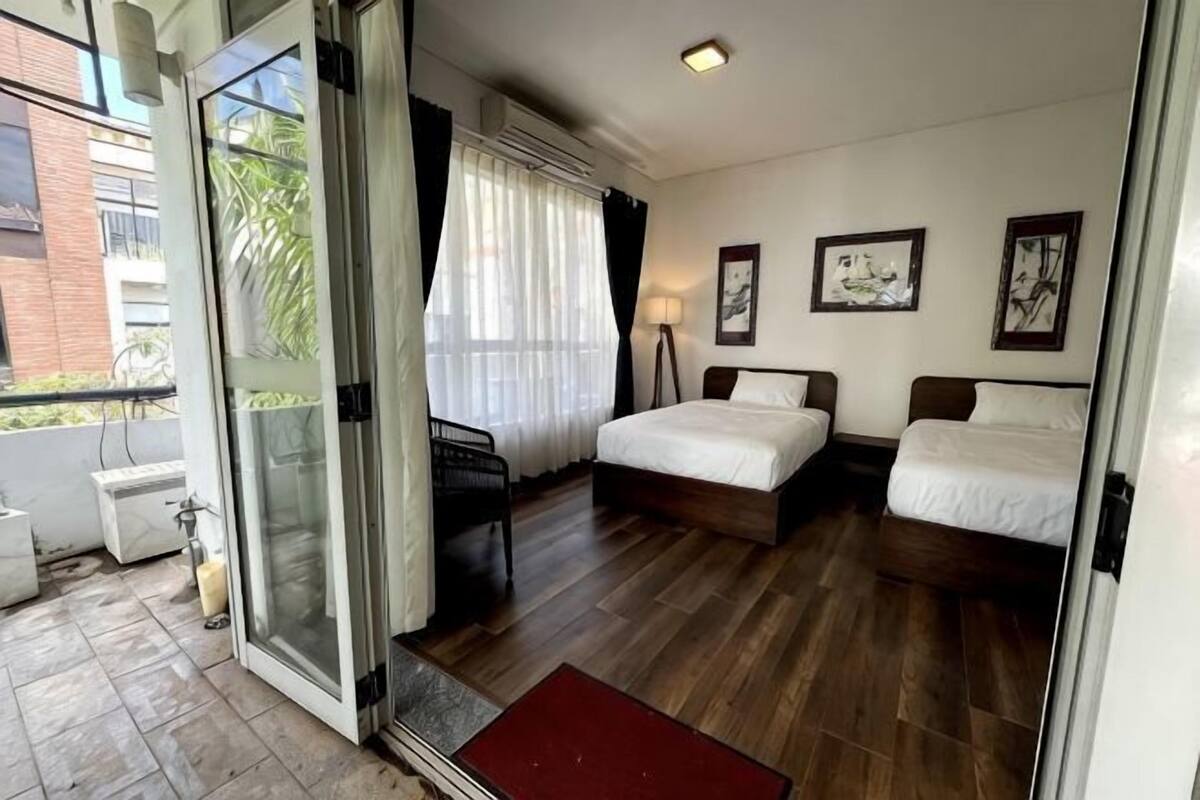 Een hotelkamer met twee bedden, een balkon en uitzicht op een gebouw.