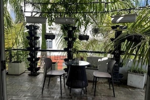 Una terrazza esterna con un tavolo rotondo e sedie, circondata da piante in vaso e una ringhiera in metallo.