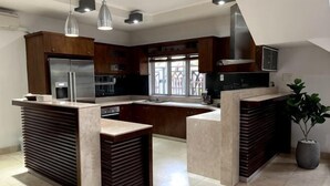 A modern kitchen with a central island, built-in appliances, pendant lighting, and a large window. - Kim’s House Entire Villa 6-BR Near My Khe Beach (Da Nang)