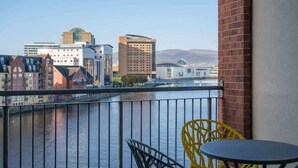 A balcony with a view of a river and buildings, featuring yellow chairs and a table. - 5-bedroom apartment with river views - Goliath (Belfast)