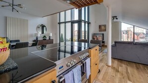 A modern kitchen with a large island, a dining area, and a living space with a view of the city. - 5-bedroom apartment with river views - Goliath (Belfast)