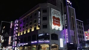 Un hôtel reconnaissable à son grand panneau « Grande ouverture », à ses nombreux étages et aux différentes enseignes commerciales qui ornent sa façade.