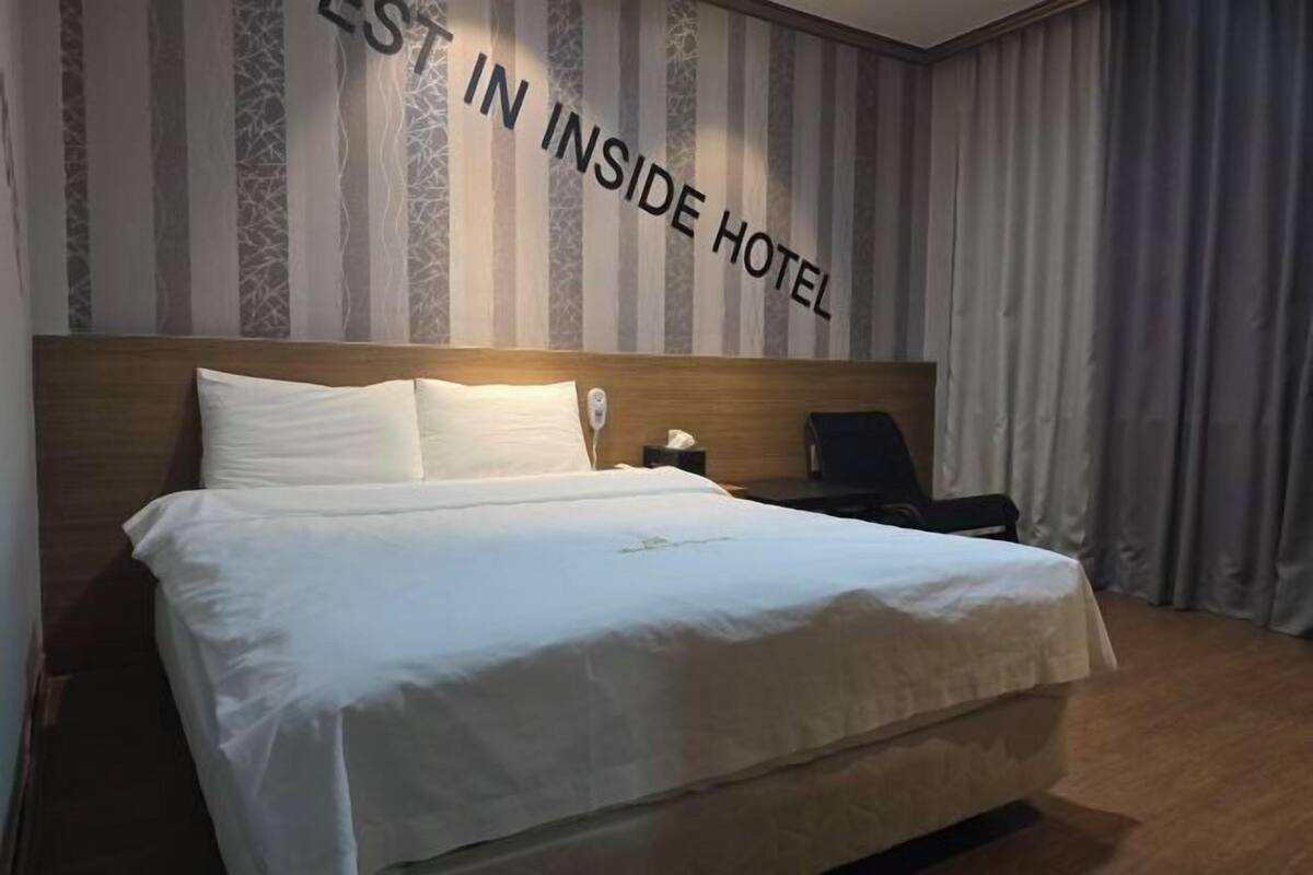 A hotel room with a large bed, a wooden headboard, a nightstand with a lamp, and a curtain.