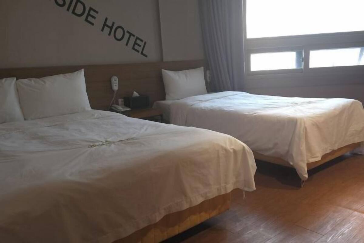 A hotel room with two beds, a wooden headboard, a bedside table with a phone, and a window with curtains.