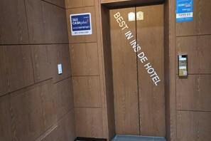 An elevator interior with a wooden wall, a sign indicating 'BEST IN INS HOTEL,' and a '345 CASH' sign. - Best in Hotel (Siheung-si)